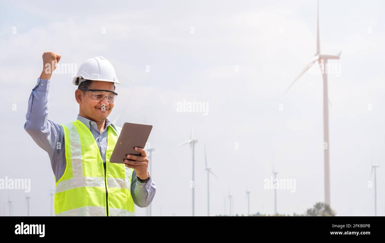 Un ingegnere di successo che utilizza una tavoletta con turbina eolica in background Foto Stock