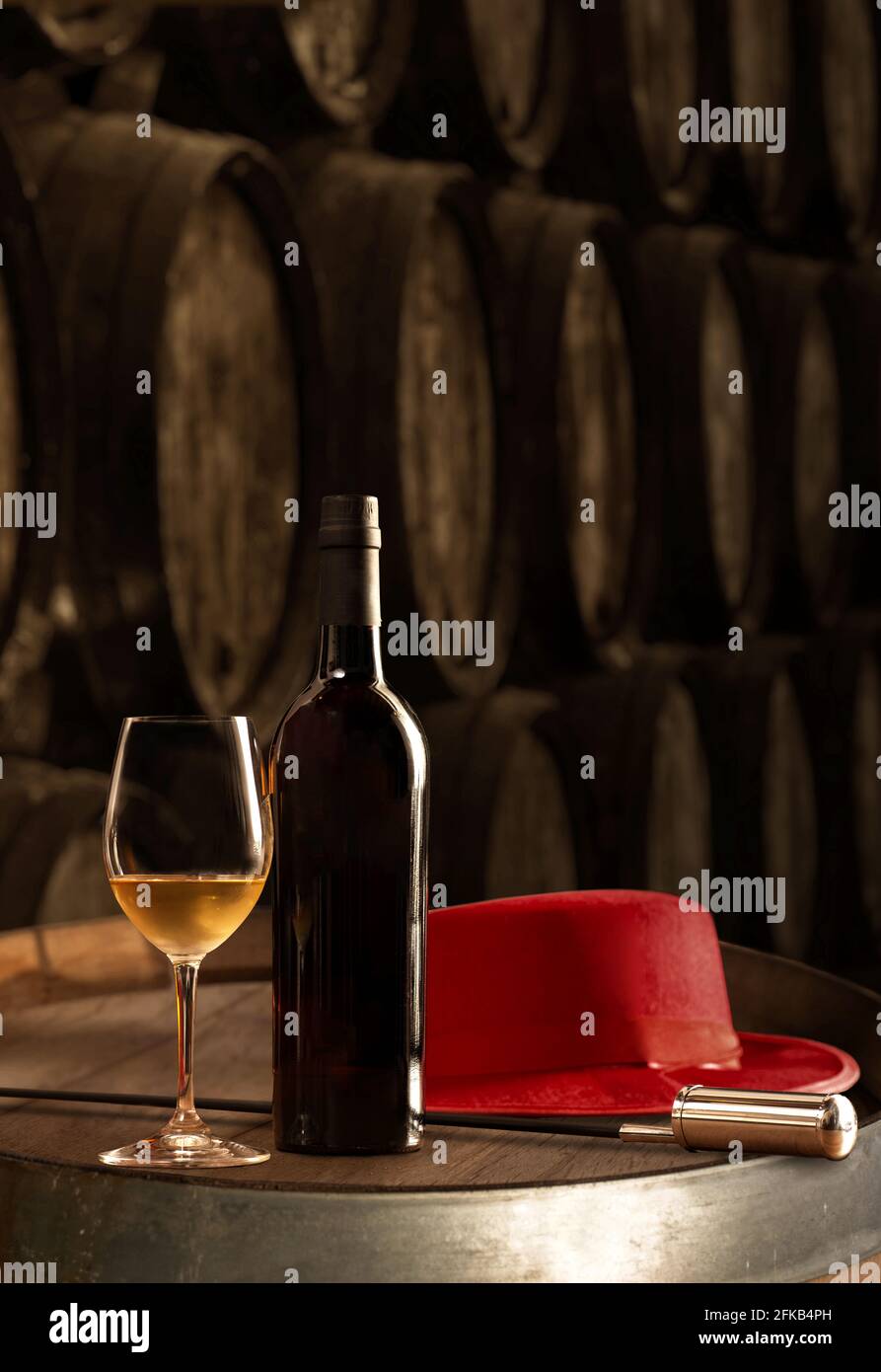 Bottiglia e bicchiere di vino fino bianco sherry in cantina Con tipico Jerez e cappello rosso veneziano sul tavolo sullo sfondo di vecchi barili vertici Foto Stock