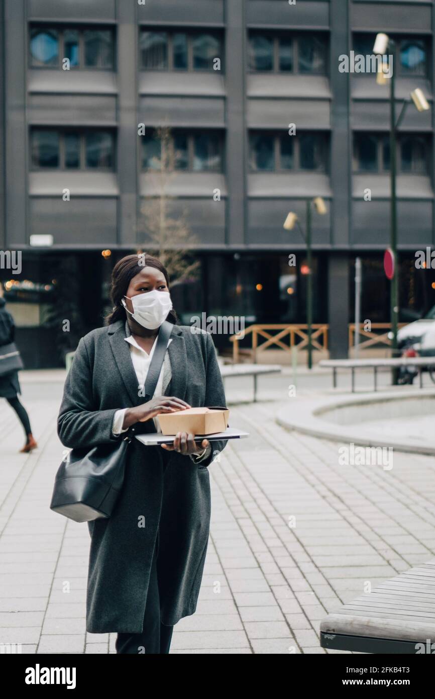 Donna d'affari con cibo confezionato e portatile a piedi nel parco ufficio durante la pandemia Foto Stock