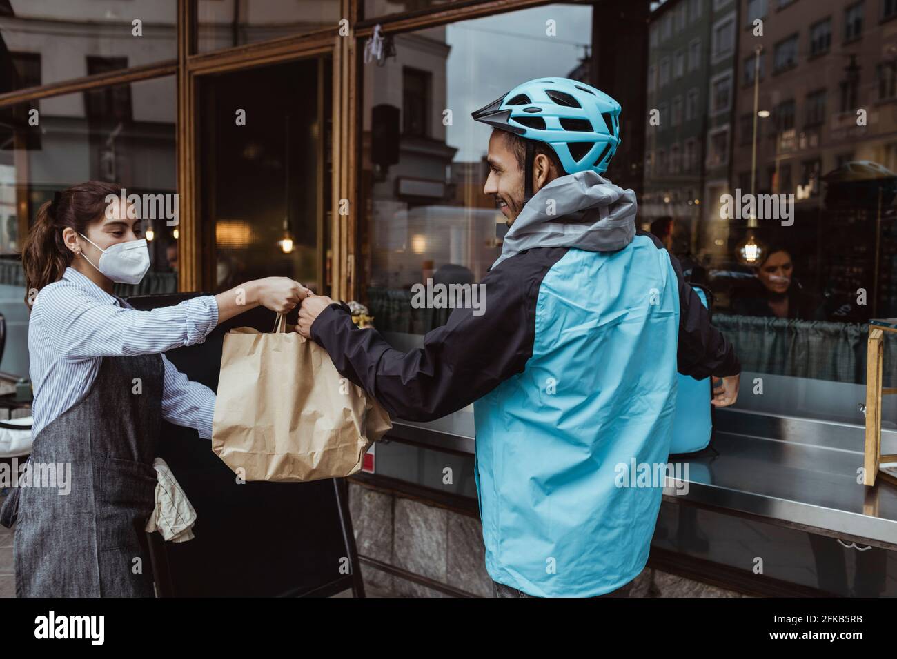 Donna che dà ordine di pacchetto a uomo di consegna fuori deli fare acquisti durante la pandemia Foto Stock