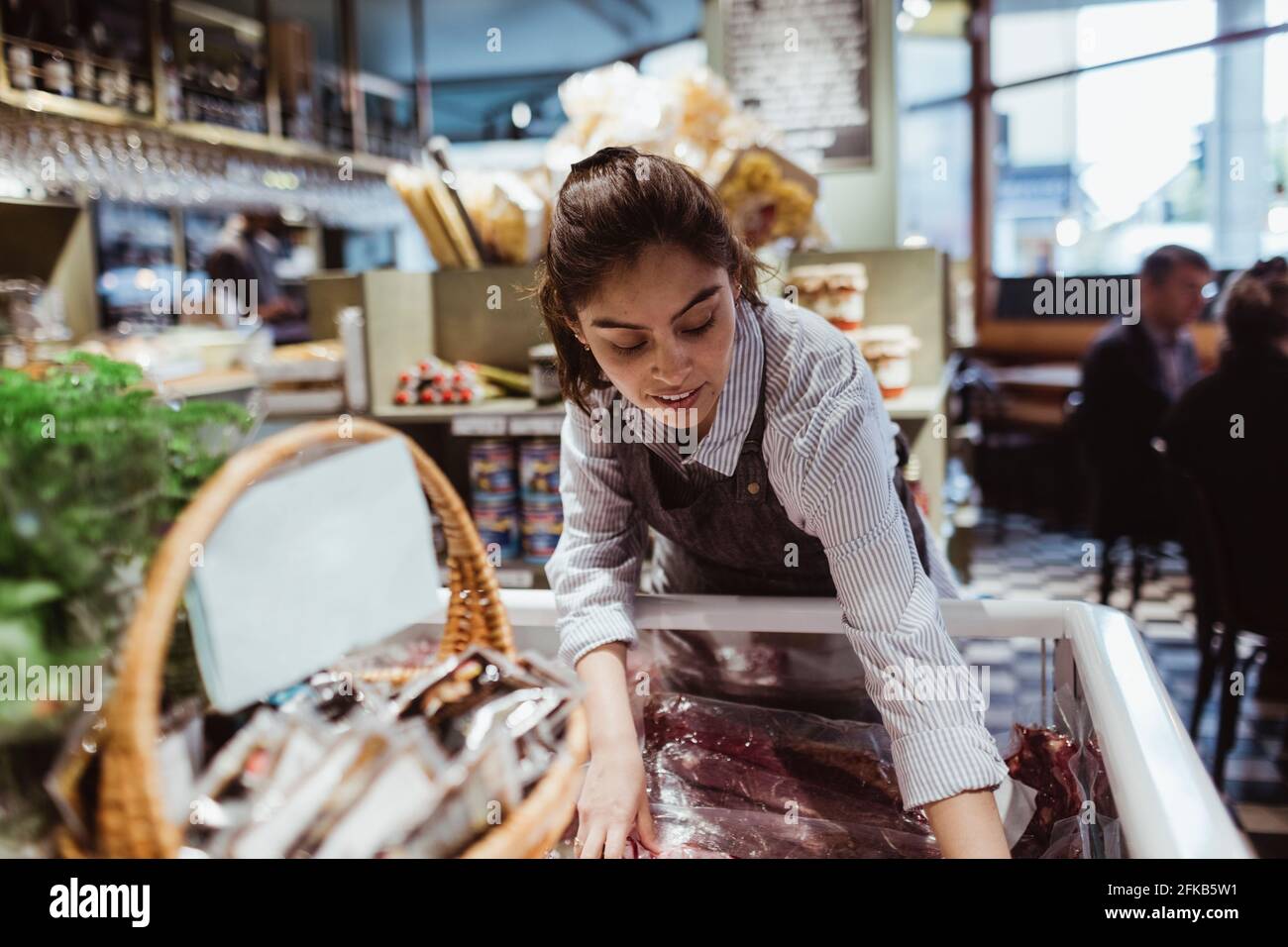 Giovane donna proprietario che organizza il cibo di pacchetto in armadietto di esposizione a. negozio Foto Stock