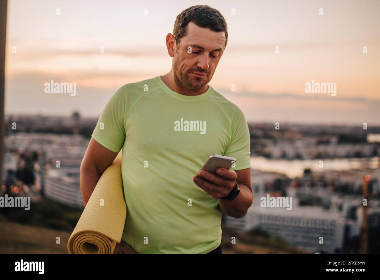 Atleta maschile maturo che usa il telefono cellulare contro il cielo durante il tramonto Foto Stock