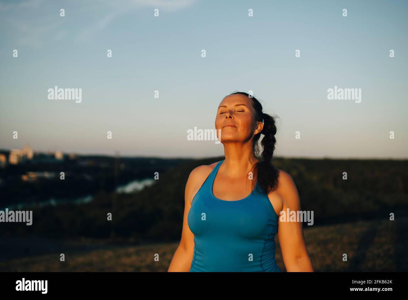 Atleta femminile con gli occhi chiusi contro il cielo durante il tramonto Foto Stock