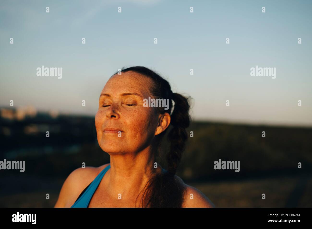 Donna sportiva con gli occhi chiusi contro il cielo durante il tramonto Foto Stock