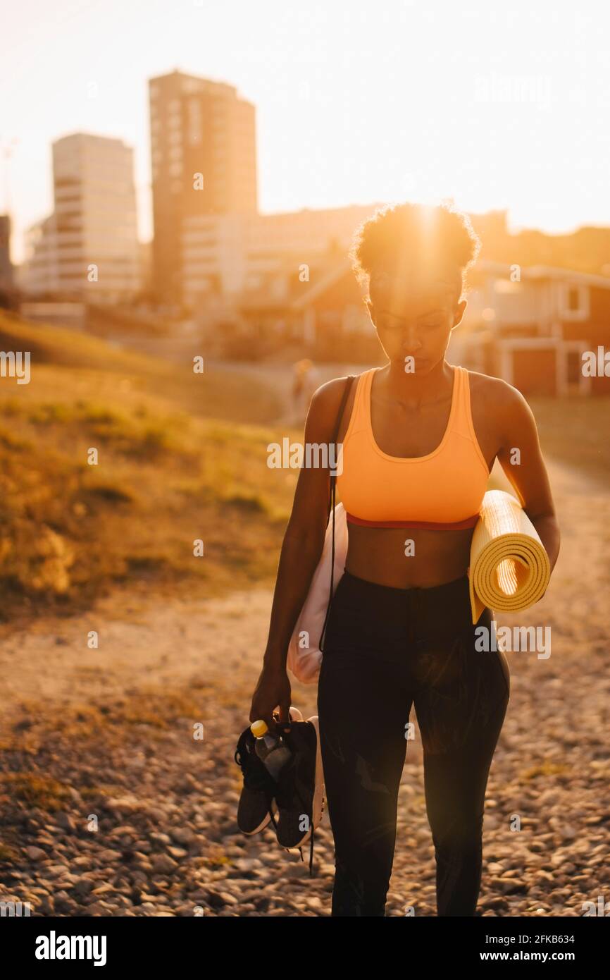 Giovane atleta con scarpe sportive e tappetino da ginnastica in piedi sulla terra durante il tramonto Foto Stock