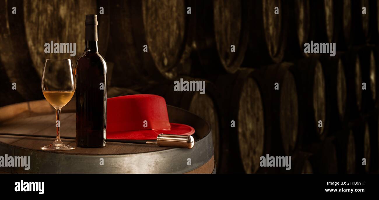 Bottiglia e bicchiere di raffinato vino di sherry bianco in cantina Con tipico Jerez e cappello rosso veneziano sul tavolo sullo sfondo del vecchio banner barili Foto Stock