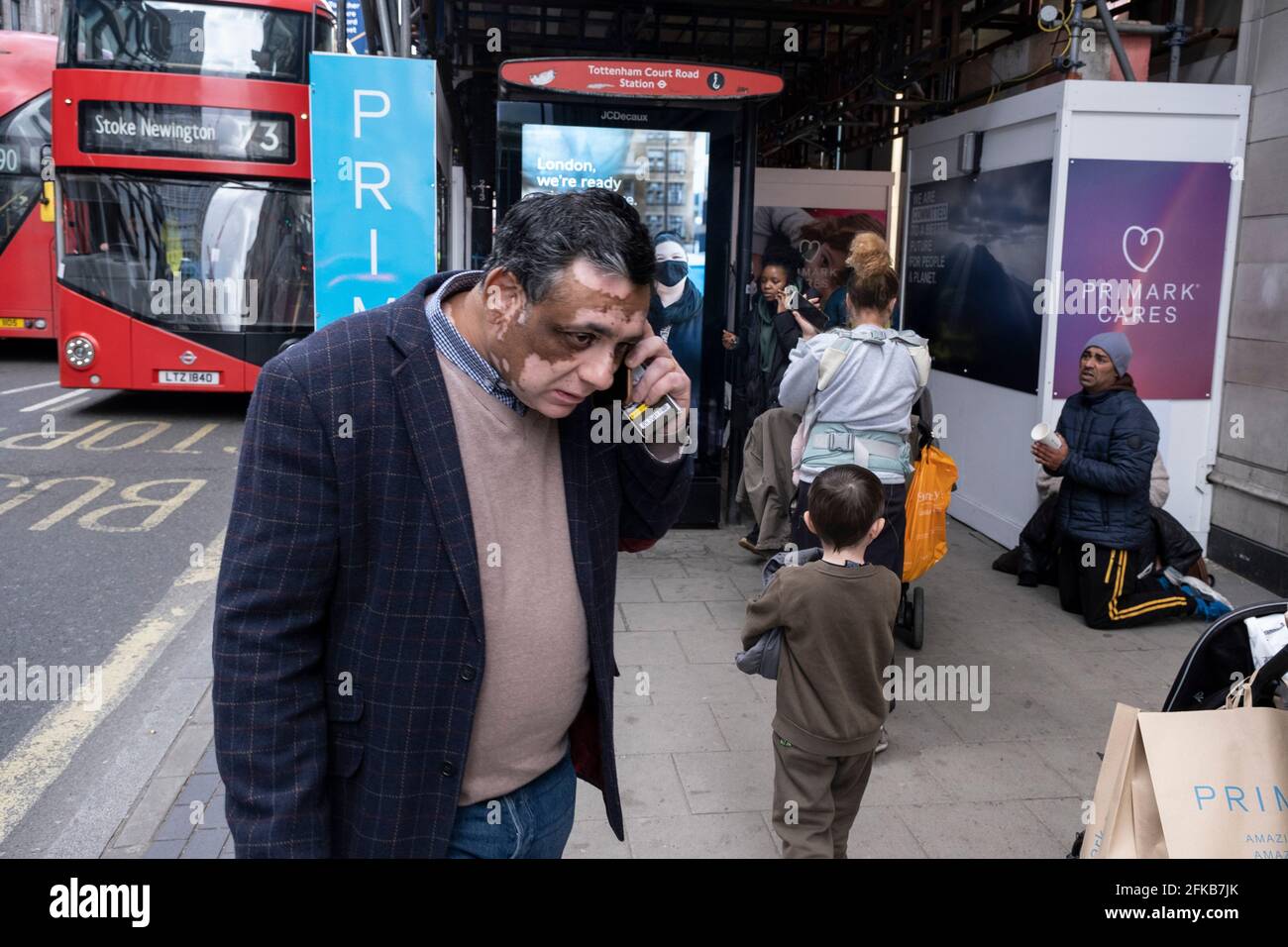 L'uomo si inginocchiò sul marciapiede pregando di denaro mentre gli acquirenti tornano a Primark su Oxford Street, mentre i negozi non essenziali riaprono e il coronavirus nazionale chiuderà tre cavalletti il 12 aprile 2021 a Londra, Regno Unito. Ora che è stata delineata la tabella di marcia per uscire dal blocco nazionale, questa è la prima fase di alleggerimento delle restrizioni, e un gran numero di persone sono fuori nel distretto commerciale di Londons per fare shopping. Foto Stock