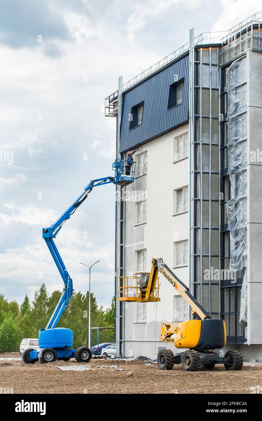 Bielorussia, Minsk - 28 maggio 2020: Un lavoratore su una piattaforma di sollevamento dipinge la facciata di un nuovo edificio urbano moderno in costruzione in un si di costruzione Foto Stock