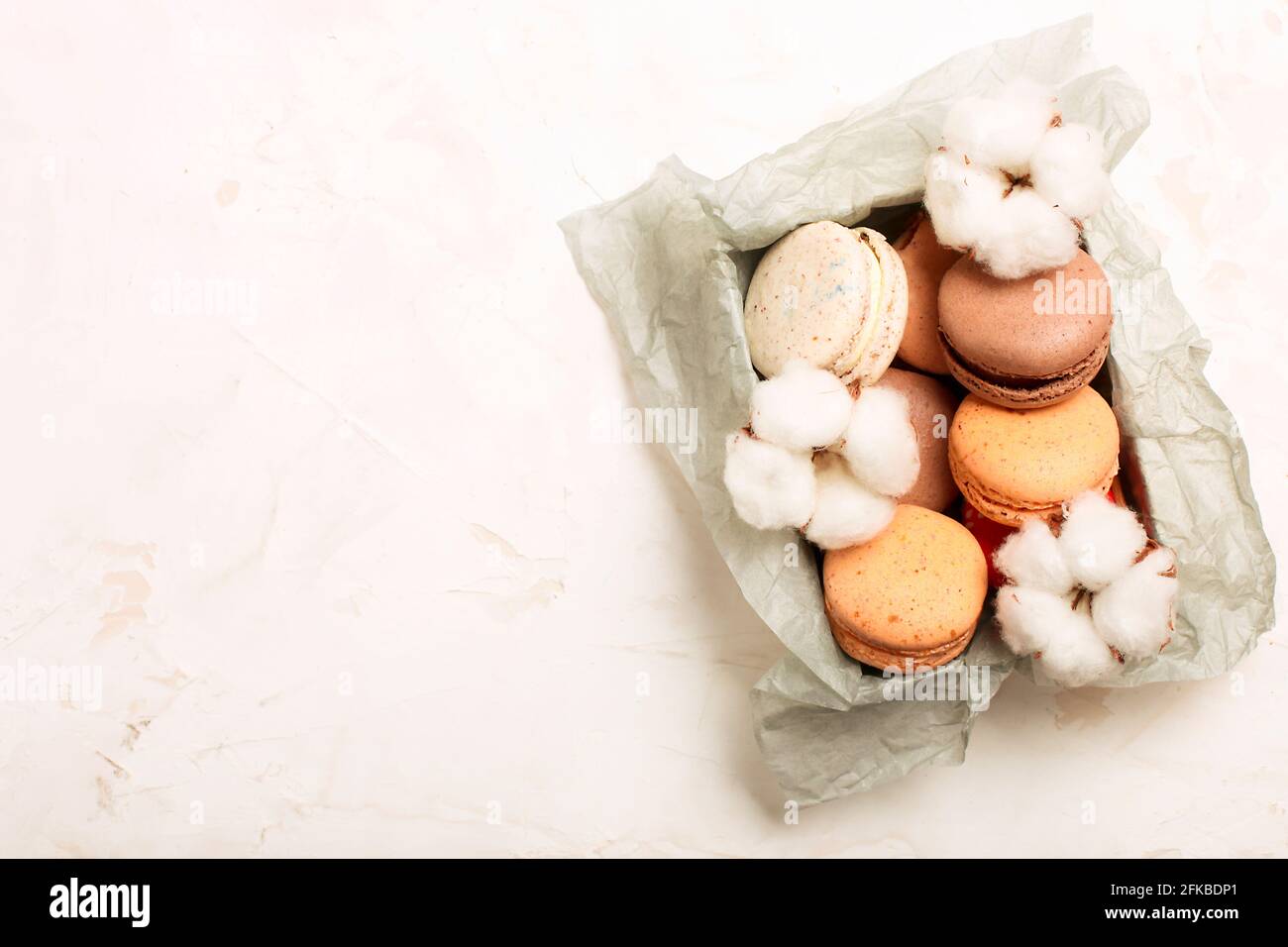 Elegante composizione di macaroni francesi in scatola e ramificazione di bol di cotone su tavola bianca in stucco testurizzata. Buon compleanno San Valentino giorno delle donne spr Foto Stock