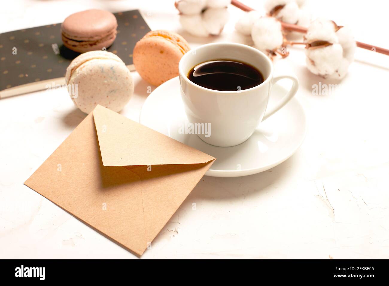 Composizione elegante, macaron al cioccolato assortiti francesi, tazza da caffè, taccuino, bol di cotone, tavolo con intonaco bianco. Buon compleanno mothe Foto Stock