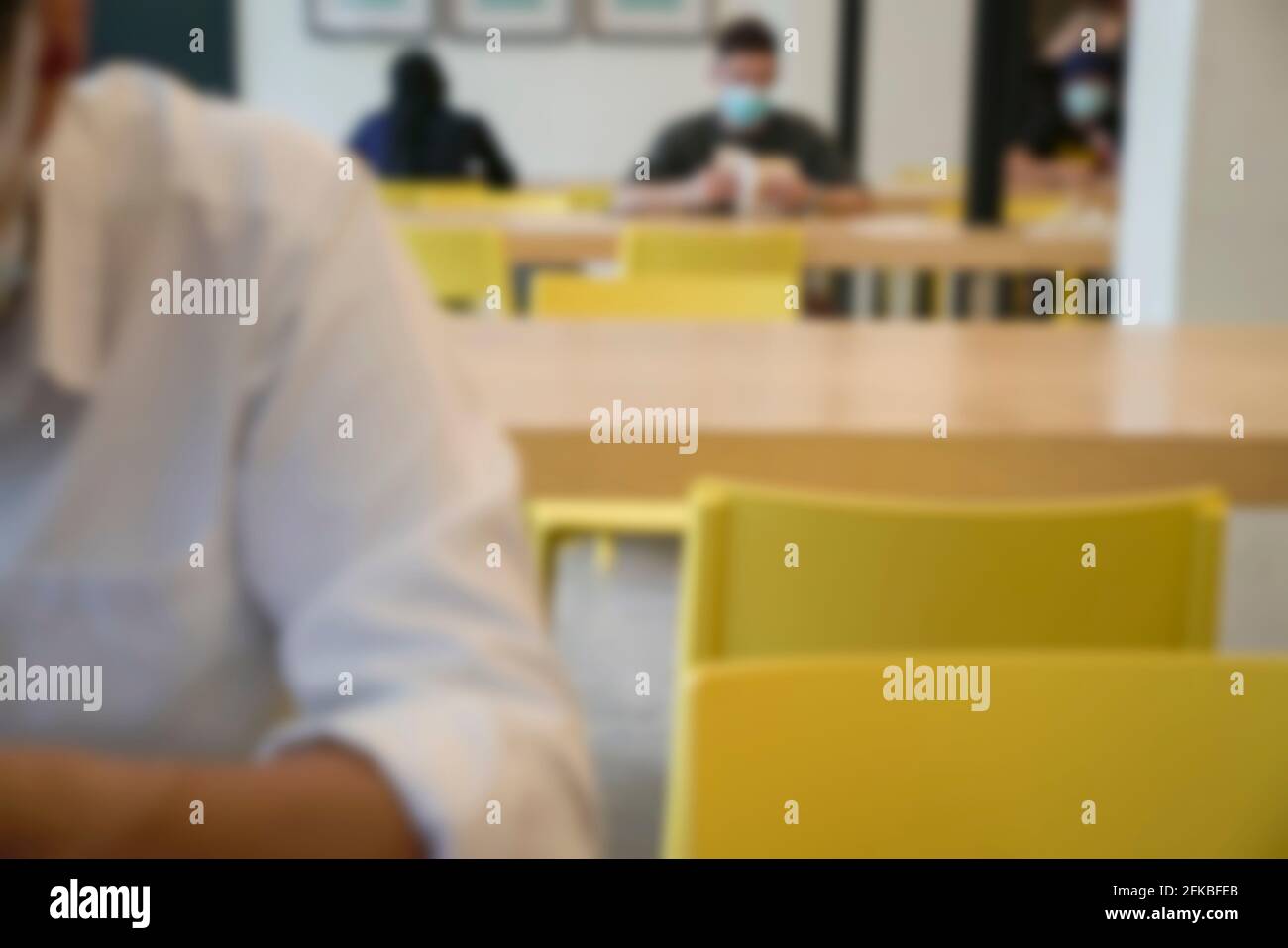 Persone che indossano la maschera seduta e la lettura sul tavolo nella biblioteca. Sfocato. Foto Stock