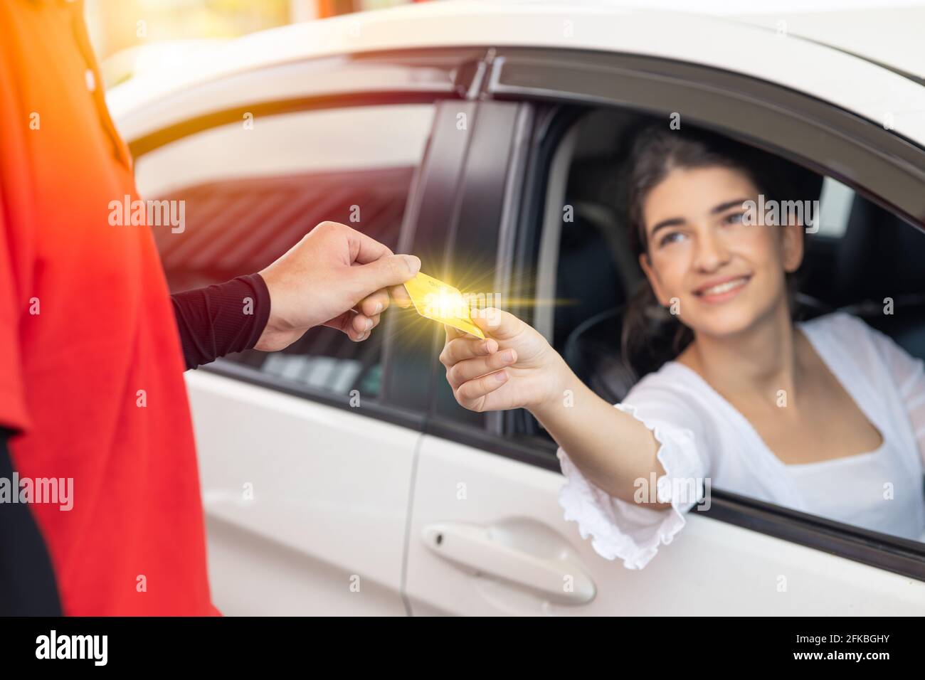 felice conducente donna cliente che dà carta di credito denaro pagamento a. personale per il costo del carburante presso la stazione di servizio o il costo del servizio in garage Foto Stock
