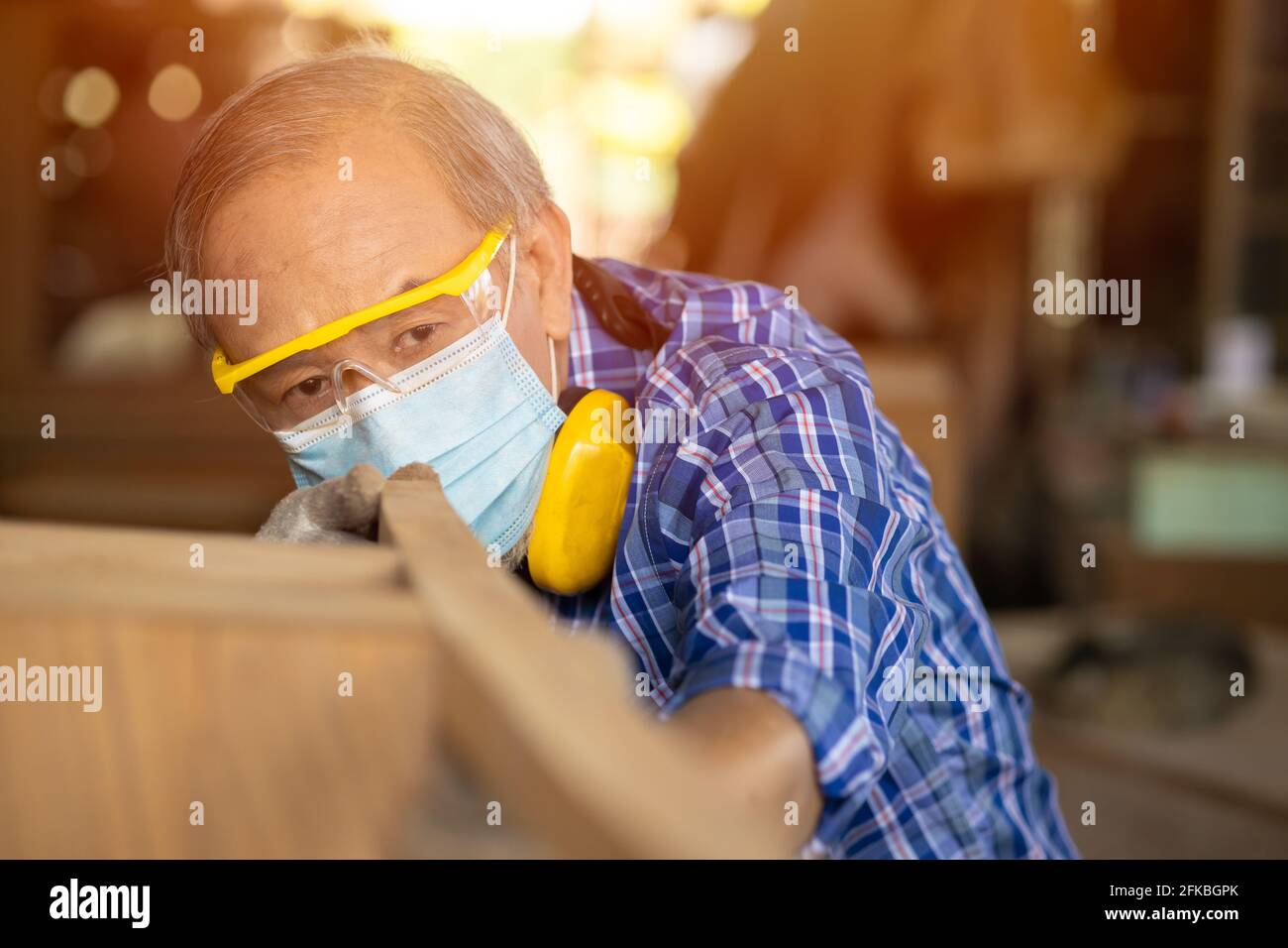 Anziano lavoratore legno woodcraft ritire hobby per il buon pensionamento, asiatico maschio maturo maestro professionale di fare mobili in legno con maschera protects viso Foto Stock