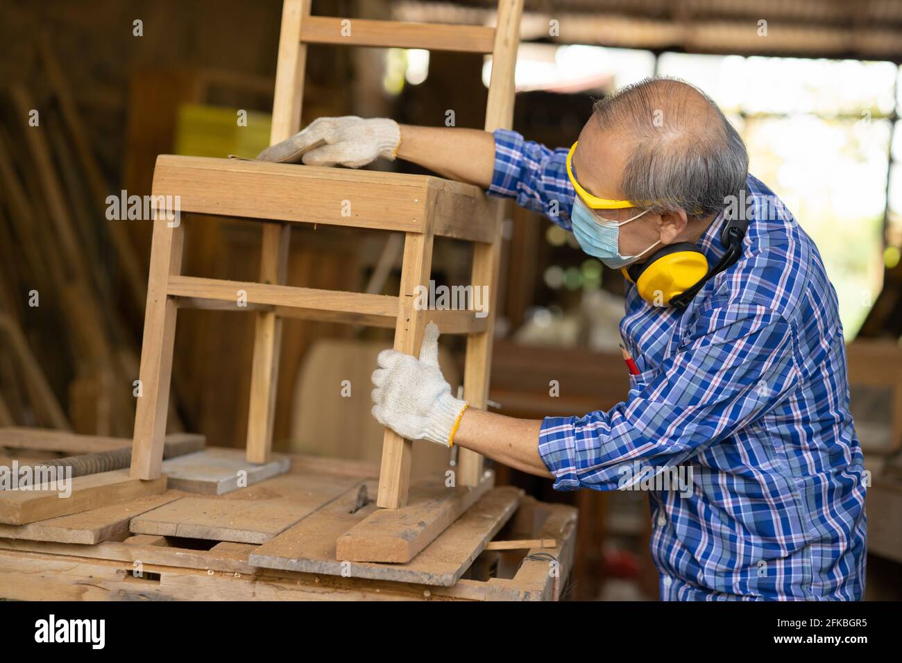 Anziano lavoratore legno woodcraft ritire hobby per il buon pensionamento, asiatico maschio maturo maestro professionale di fare mobili in legno con maschera protects viso Foto Stock