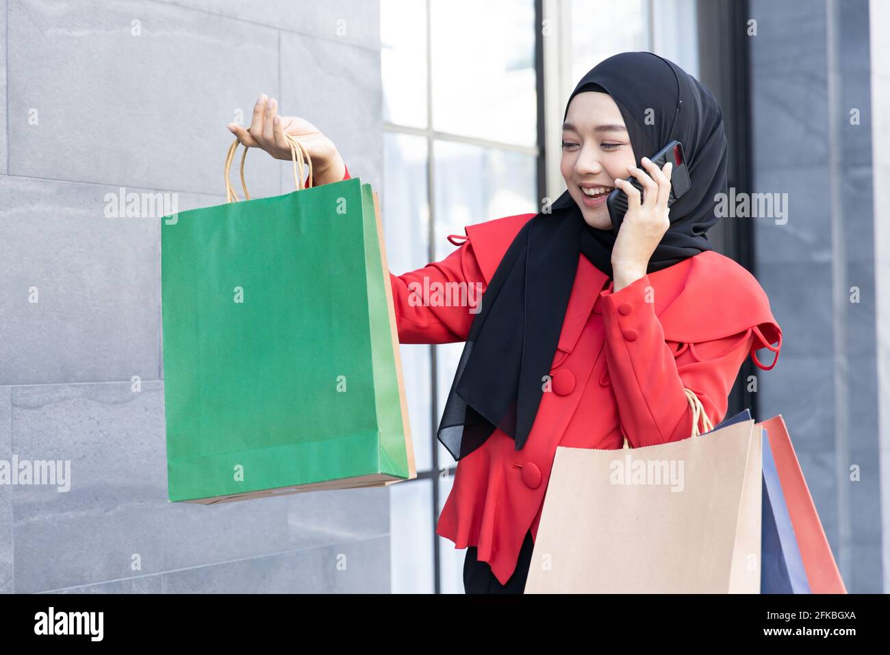 Stile di vita moderno della giovane donna musulmana araba in velo hijab con borse per lo shopping a piedi sulla strada dello shopping telefono chiamata. Foto Stock