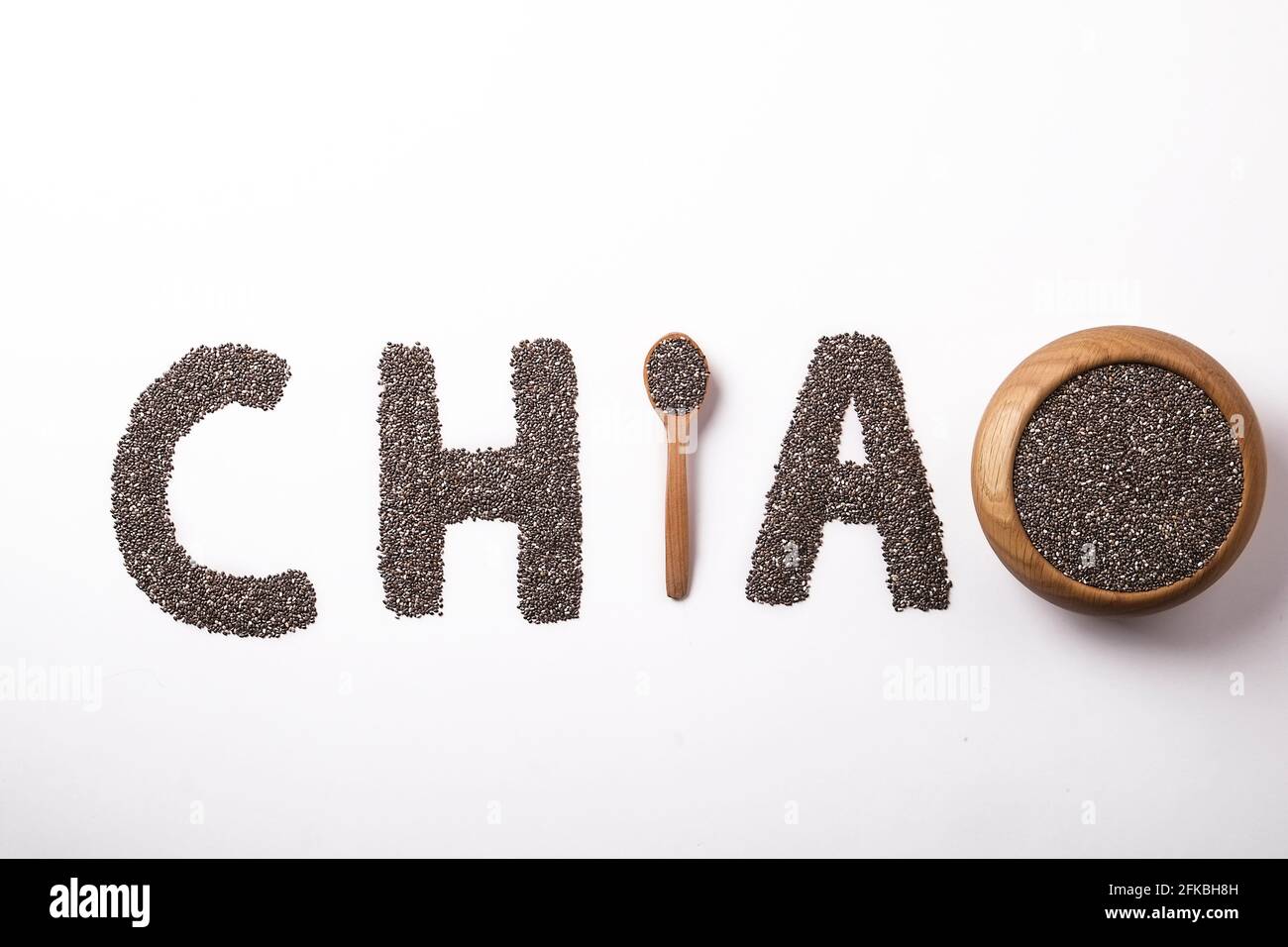 Parola chia scritto con semi neri e cucchiaio di legno, isolato su superficie bianca con ciotola. Concetto di cibo pulito. Supplemento alimentare vegano, supercibo. C Foto Stock