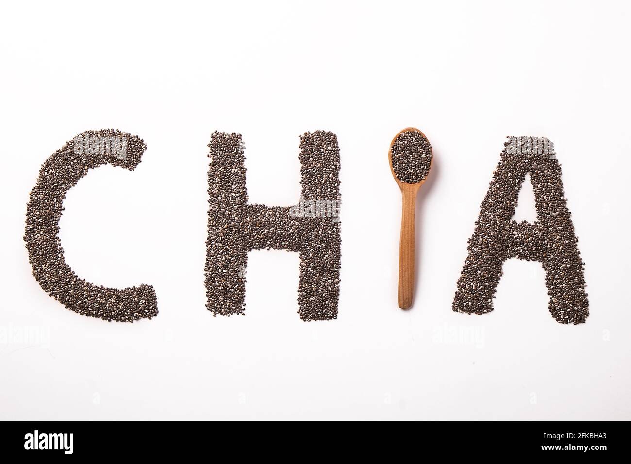 Parola chia scritto con semi neri e cucchiaio di legno, isolato su superficie bianca con ciotola. Concetto di cibo pulito. Supplemento alimentare vegano, supercibo. C Foto Stock