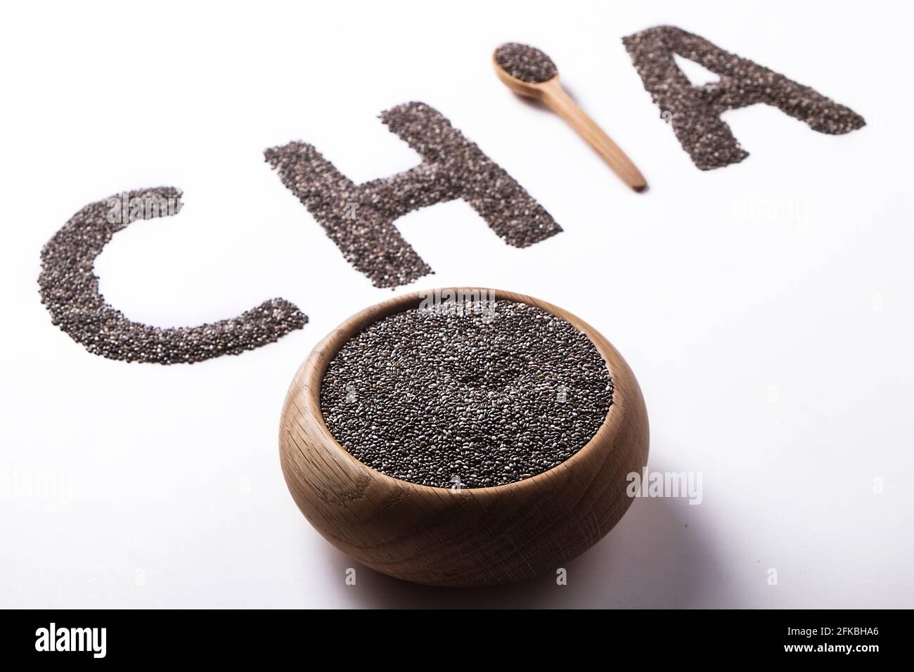 Parola chia scritto con semi neri e cucchiaio di legno, isolato su superficie bianca con ciotola. Concetto di cibo pulito. Supplemento alimentare vegano, supercibo. C Foto Stock