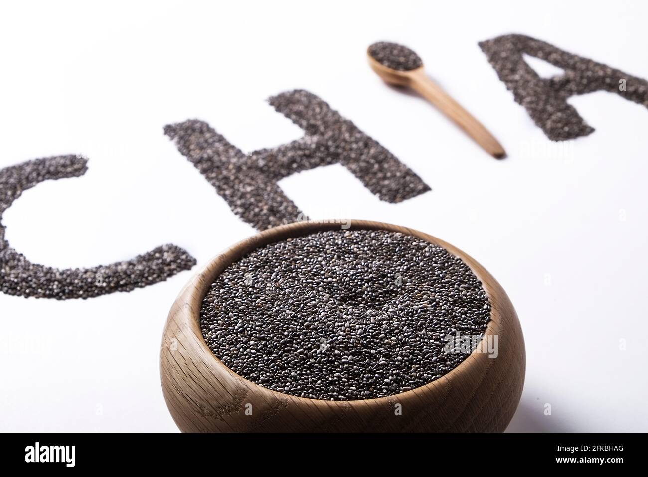 Parola chia scritto con semi neri e cucchiaio di legno, isolato su superficie bianca con ciotola. Concetto di cibo pulito. Supplemento alimentare vegano, supercibo. C Foto Stock
