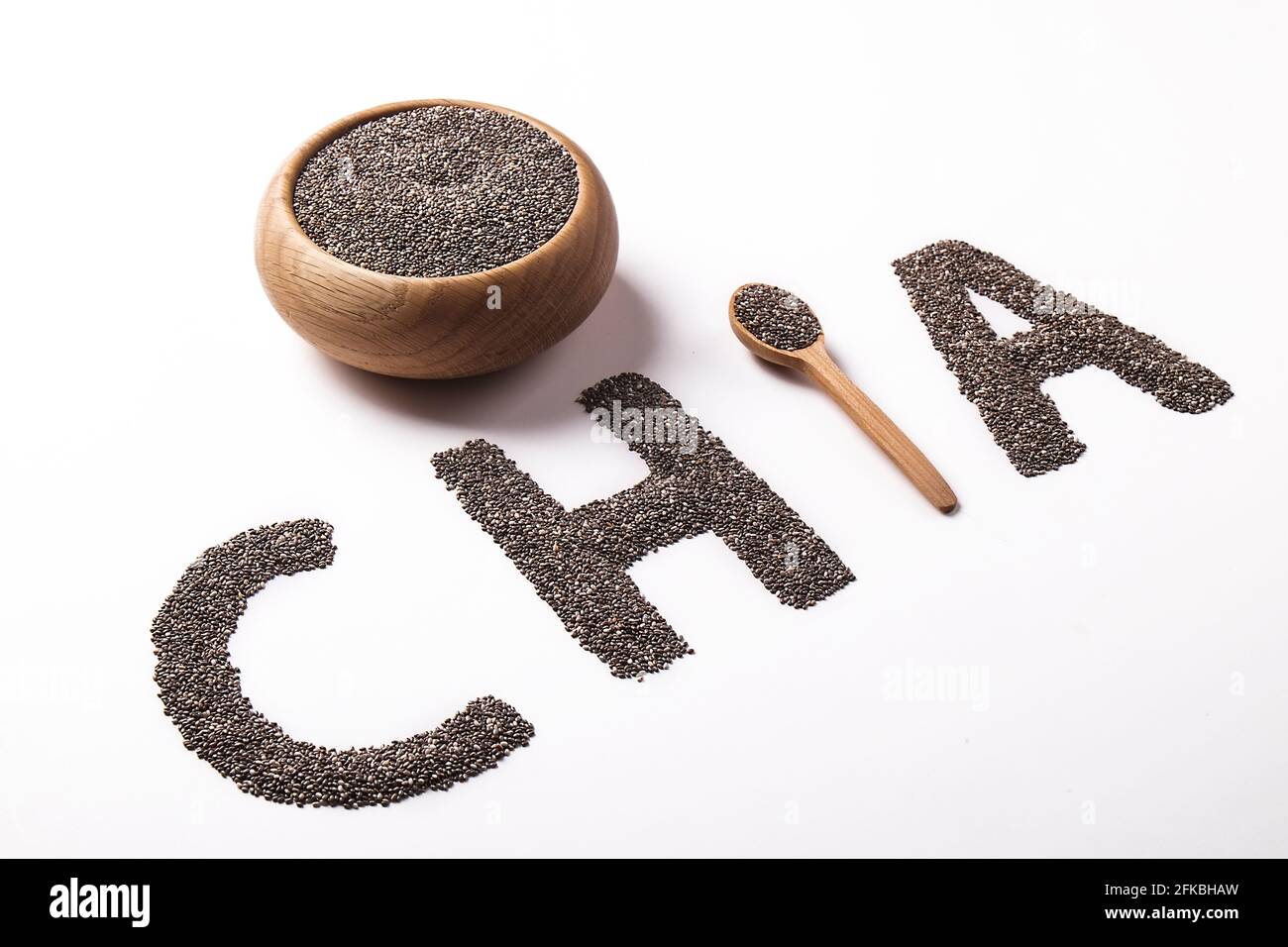 Parola chia scritto con semi neri e cucchiaio di legno, isolato su superficie bianca con ciotola. Concetto di cibo pulito. Supplemento alimentare vegano, supercibo. C Foto Stock