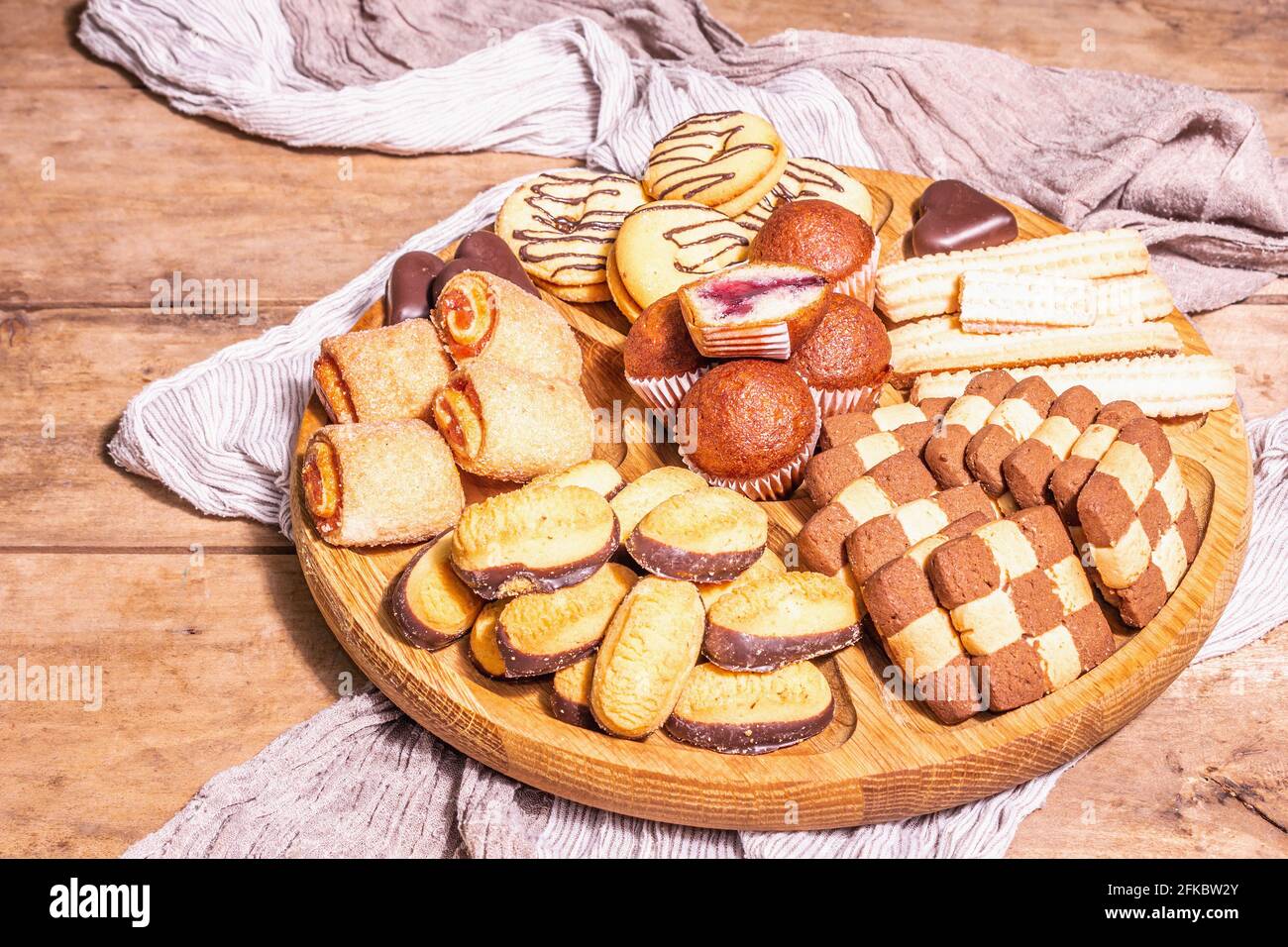 Vari biscotti e muffin assortiti. Luce dura alla moda, ombra scura. Piastra di combinazione di legno su vecchio tavolo di tavole, primo piano Foto Stock