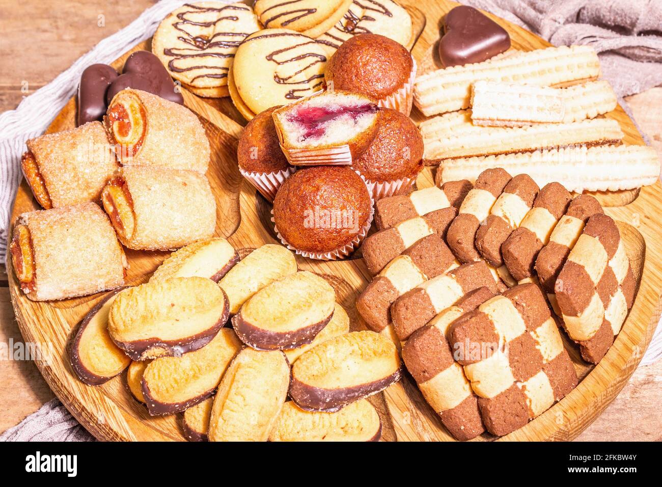 Vari biscotti e muffin assortiti. Luce dura alla moda, ombra scura. Piastra combinata in legno su vecchio tavolo in tavole, vista dall'alto Foto Stock