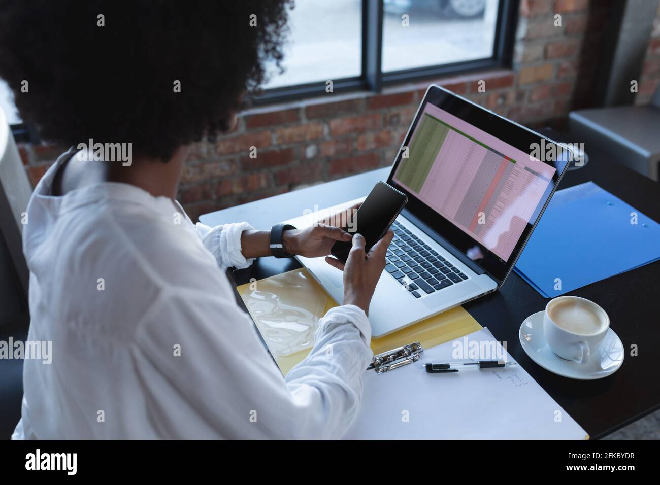 Donna afroamericana seduto in un bar utilizzando smartphone e computer portatile Foto Stock
