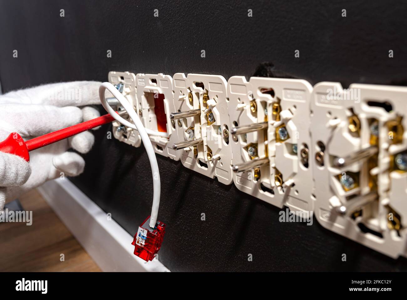 Un cavo di rete che sporge dalla parete con un modulo RJ45 pronto alla presa del computer nella stanza, prese elettriche visibili. Foto Stock