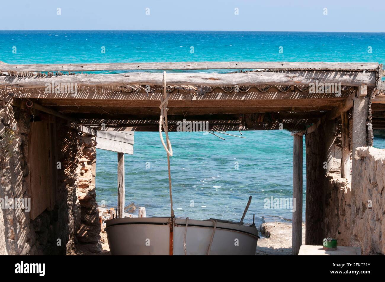 Una piccola barca su rotaie sulla spiaggia rocciosa. Barche sulle caratteristiche rotaie di legno sull'isola di Formentera. Sullo sfondo il Mediterraneo Foto Stock