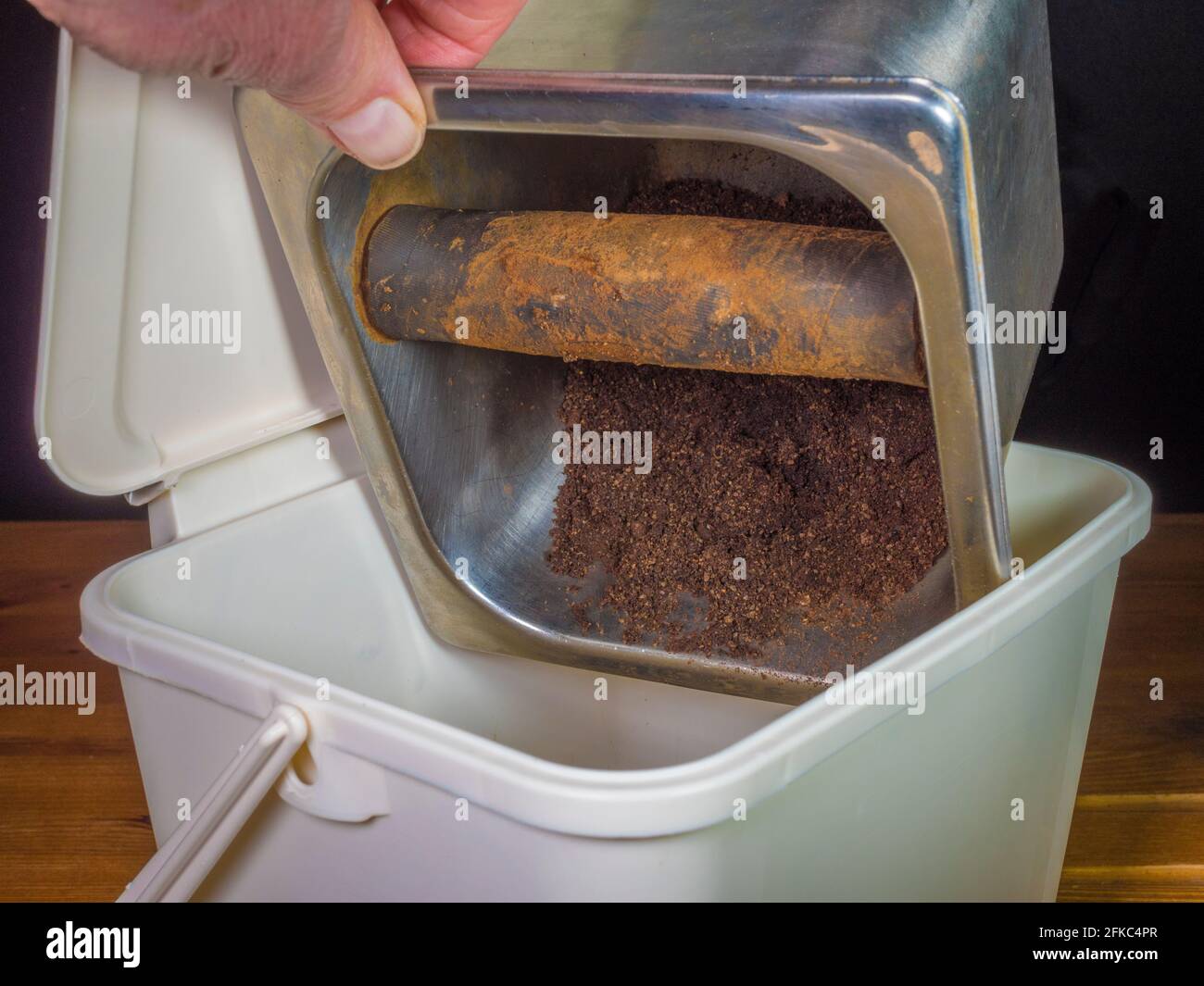 Chiudere il colpo POV di una mano di un uomo che capovolga i terreni/i macinacaffè di caffè da un contenitore di rifiuti commerciali in un piccolo bidone di plastica della cucina di compostaggio. Foto Stock