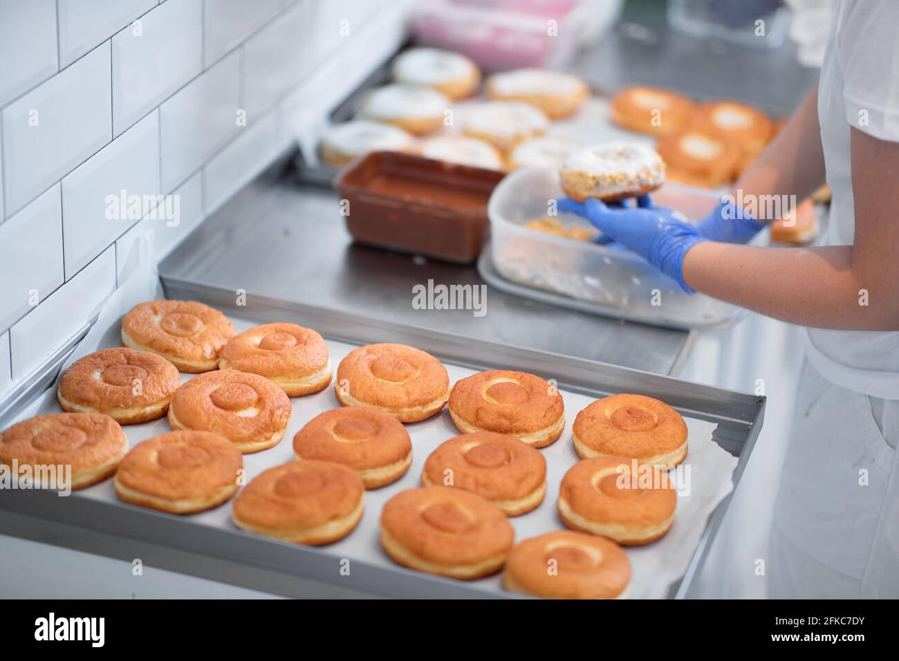 Un lavoratore spruzza ciambelle con biscotti sbriciolati in un'atmosfera di lavoro in un laboratorio di caramelle. Pasticceria, dessert, dolce, fare Foto Stock