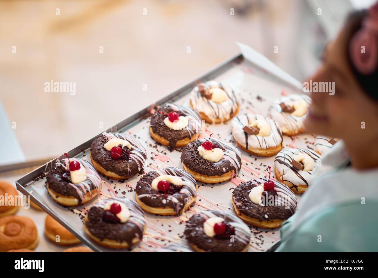 Primo piano di un vassoio pieno di deliziose ciambelle fatte a mano di irresistibilità aspetto pronto per una pasticceria tenuta da una piccola donna di affari felice proprietario. Foto Stock