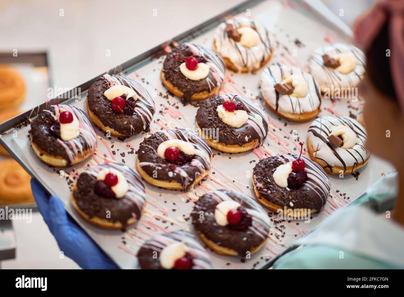 Una giovane piccola impresa donna proprietario è in possesso di un vassoio pieno di deliziose ciambelle fatte a mano di irresistibilità aspetto pronto per una pasticceria. Pasticceria, Foto Stock