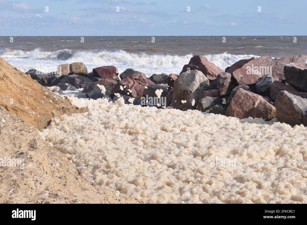 Schiuma di mare che si costruisce dietro l'armatura di roccia a Happisburgh, nord Norfolk Inghilterra UK Foto Stock