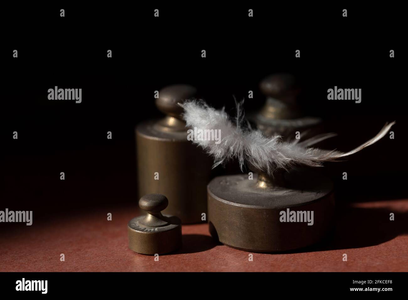 Diversi pesi metallici si trovano di fronte a uno sfondo scuro con spazio per il testo e sopra di esso si trova un bianco piuma d'uccello Foto Stock