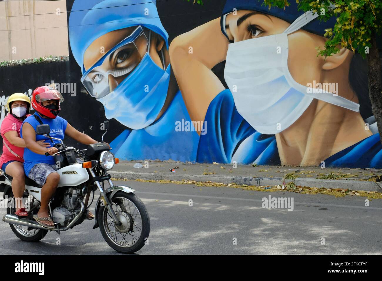 Persone che indossano maschere sul viso di una moto, con sfondo di Covid-19 Mural, Merida Messico Foto Stock