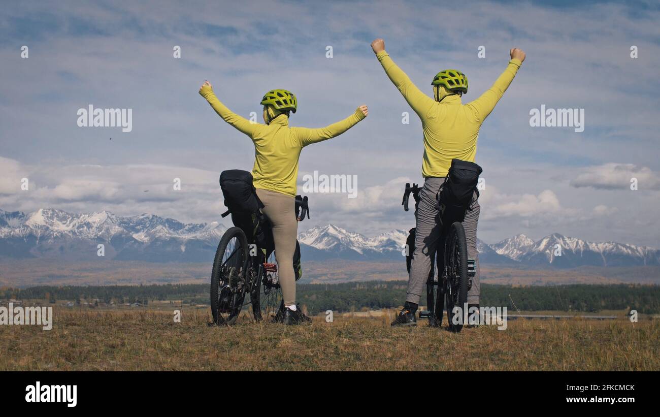 L'uomo e la donna viaggiano in bicicletta su terreni misti con bikepacking. Il viaggio di coppia di amore con tenda dentro con le borse della bicicletta. Abbigliamento sportivo elegante. Foto Stock
