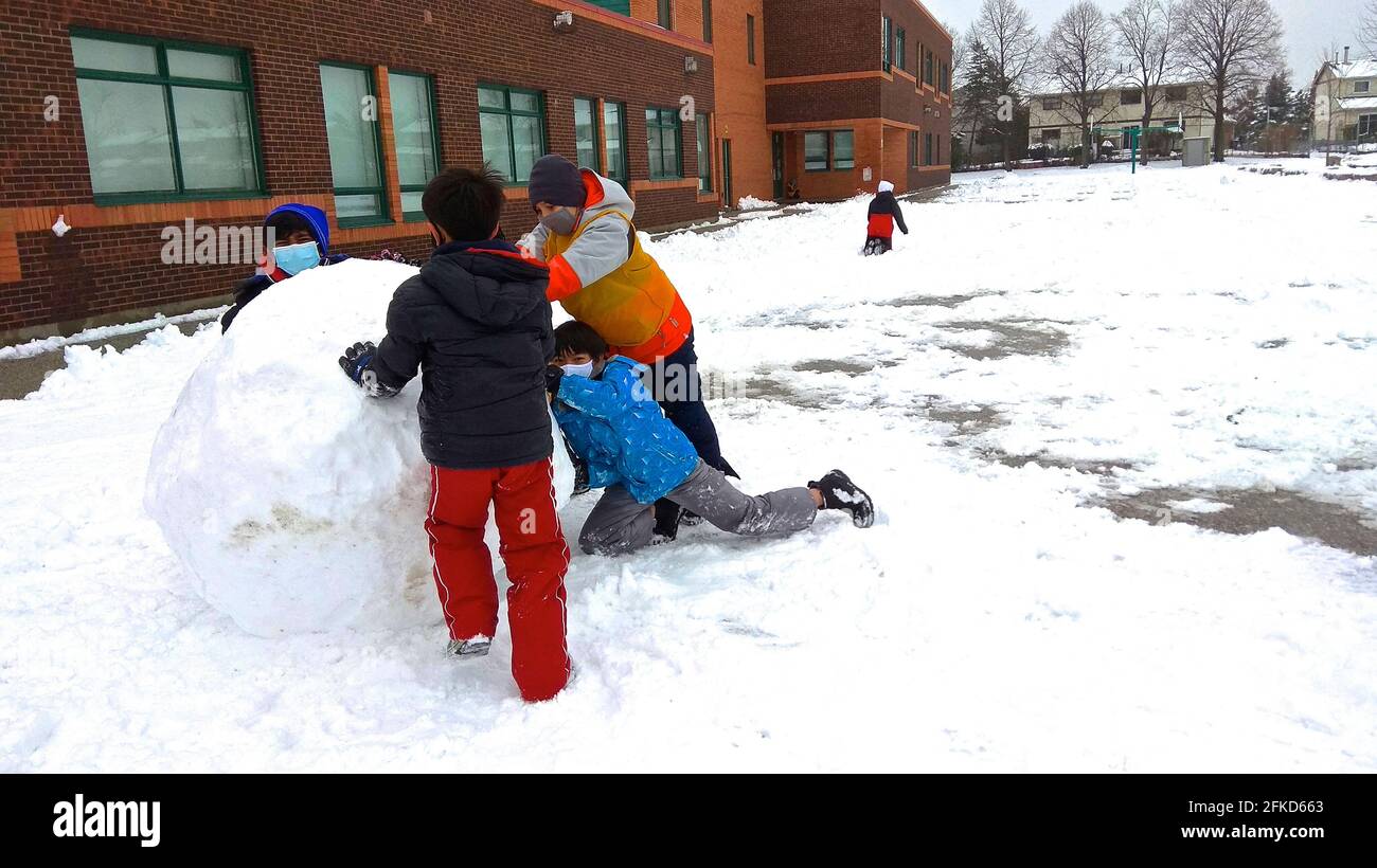 Toronto, ONT., Canada - 12/09/2020: Bambini con maschera facciale che fanno la palla di neve nel cortile della scuola durante il Covid 19 Foto Stock