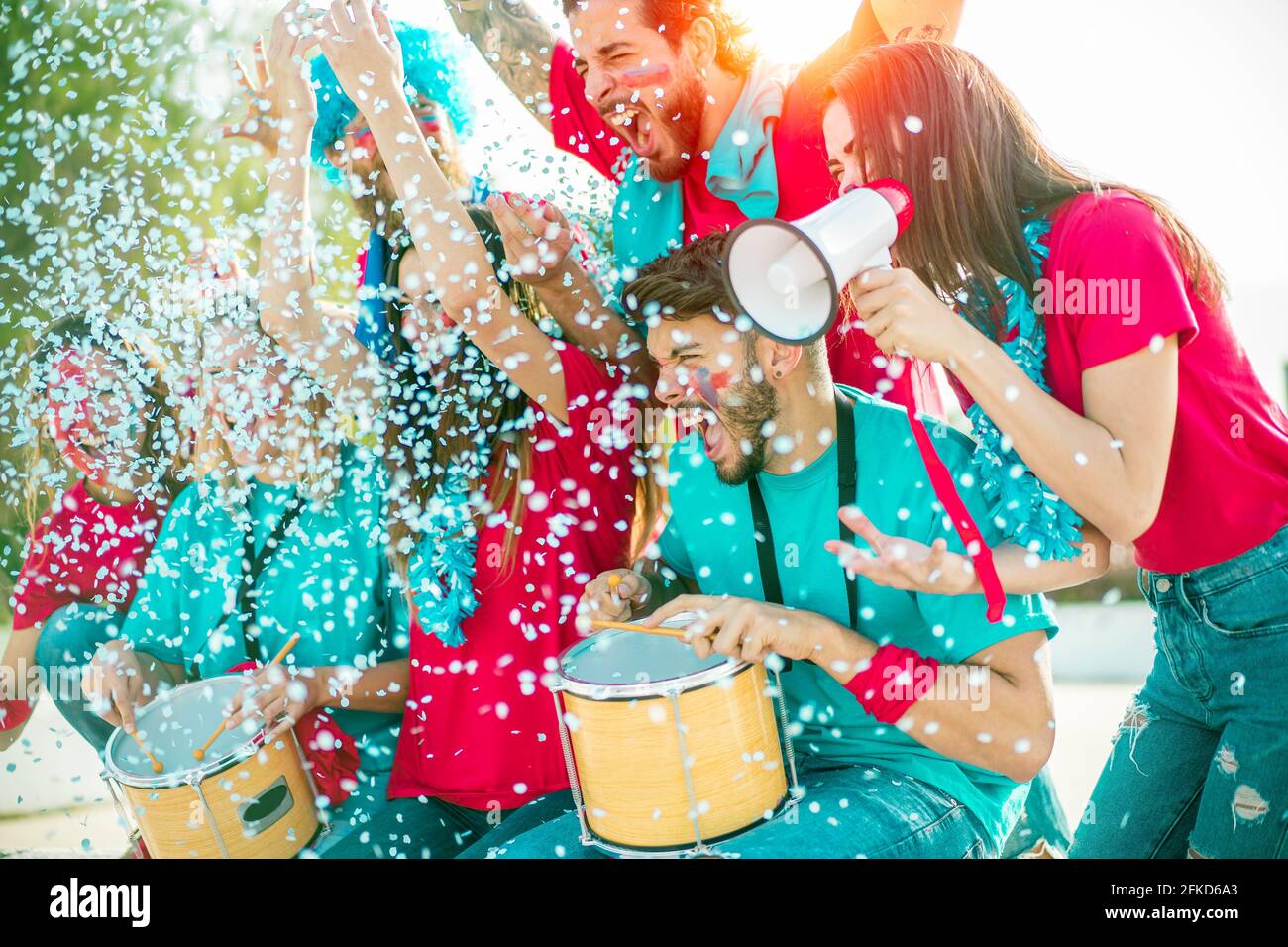 Gruppo di tifosi vestiti di rosso e blu guardando un evento sportivo negli stand di uno stadio. Amici tifosi di calcio tifosi con confetti Foto Stock