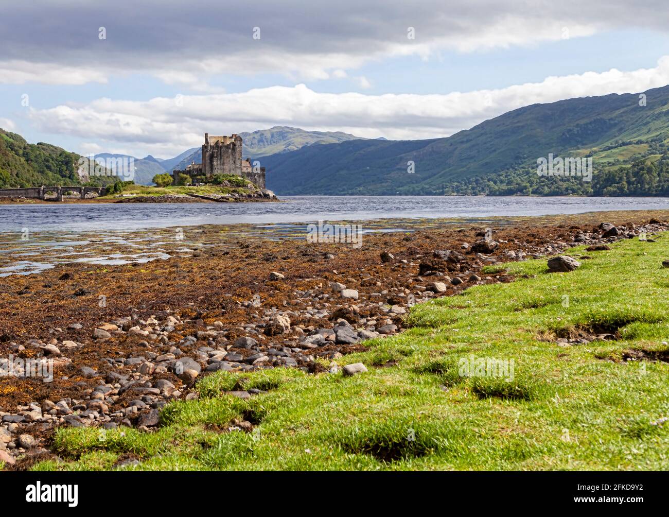 Un castello sulla cima di un campo erboso coperto con Eilean Donan sullo sfondo Foto Stock