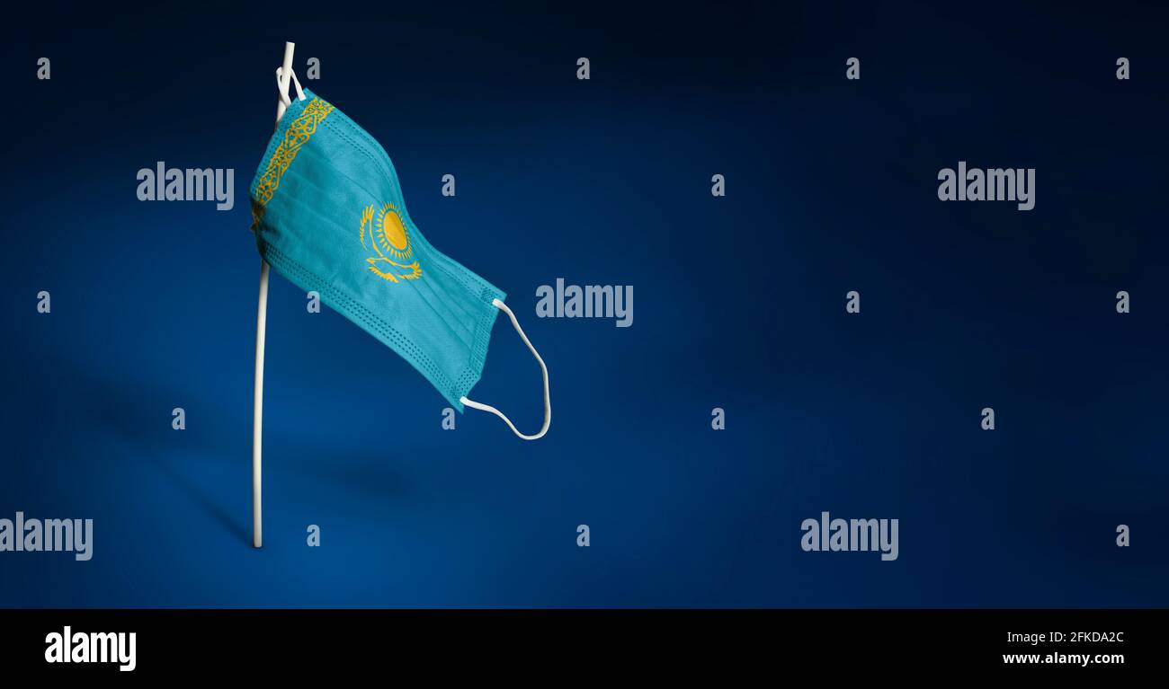 Maschera Kazakhstan su sfondo blu scuro. Bandiera ondulata del Kazakhstan dipinta su maschera medica sul palo. Concetto della bandiera della lotta contro il Foto Stock