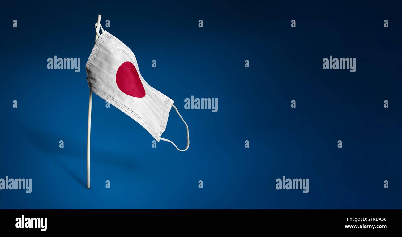 Maschera giapponese su sfondo blu scuro. Bandiera ondulata del Giappone dipinta su maschera medica sul palo. Concetto del banner della lotta contro l'epidemia Foto Stock
