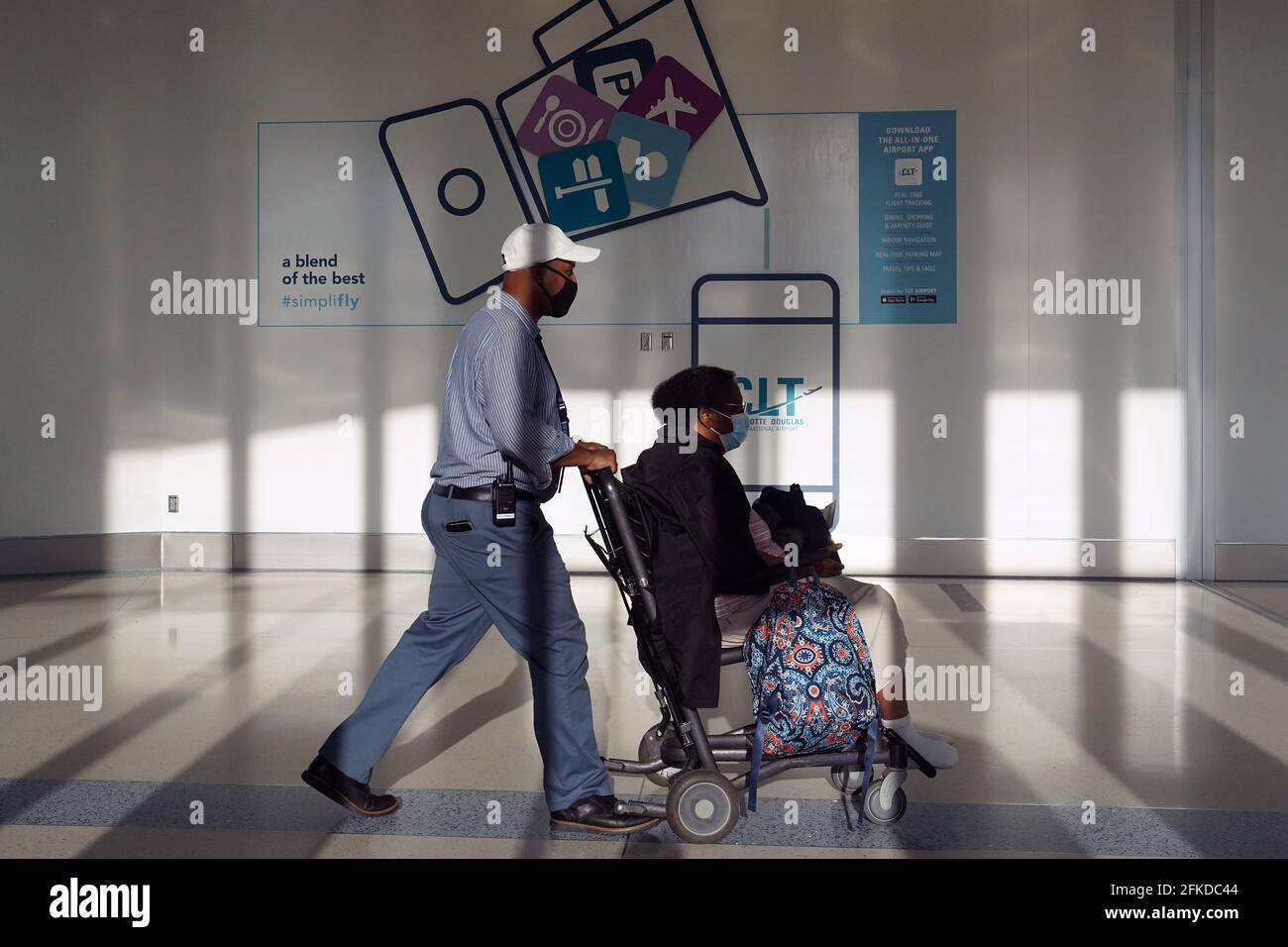 Un uomo spinge una donna in una carriola nel terminal A Concourse dell'aeroporto internazionale Charlotte Douglas, venerdì 30 aprile 2021, a Charlotte Foto Stock