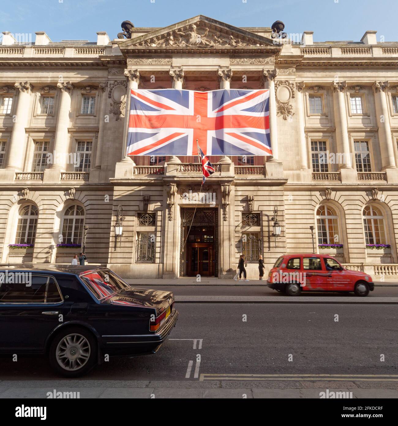 Londra, Greater London, England - Apr 24 2021: Union Jack in mostra al Pall Mall riflettendo nella finestra posteriore di un'auto come passa un taxi rosso. Foto Stock