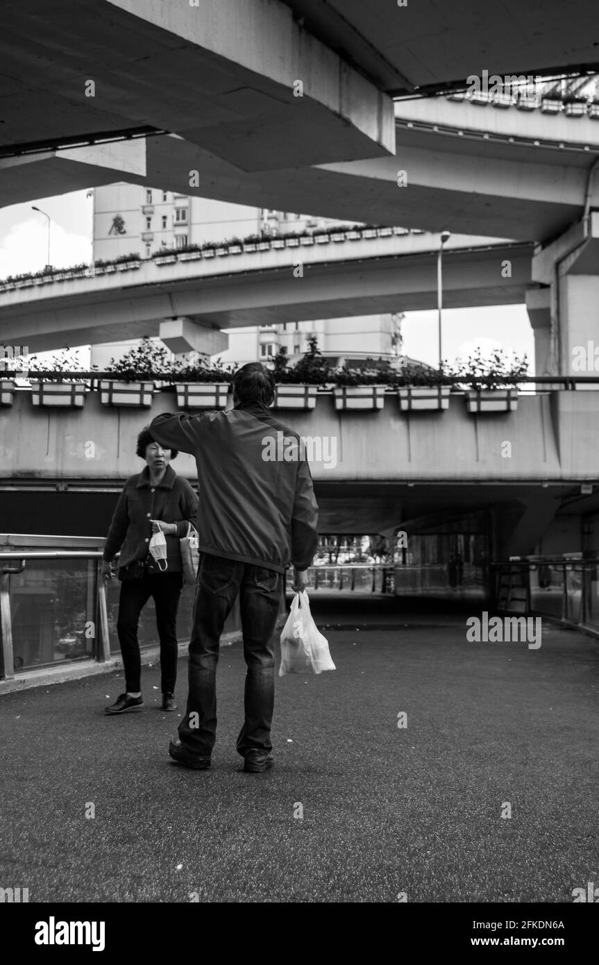 Una vecchia coppia incorniciata dalle strade sopraelevate che attraversano Yan’an East Road su un ponte pedonale nel centro di Shanghai, in Cina. Foto Stock