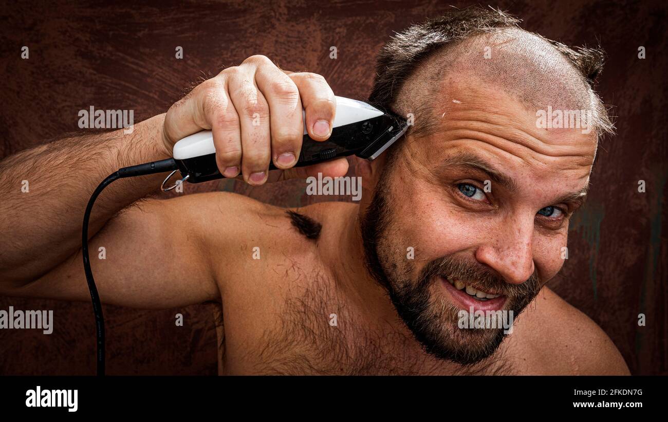 Uomo caucasico cercando di radere la testa con un rasoio elettrico. Un  brutale uomo calvo tiene un rasoio in mano e rade i peli corti su uno  sfondo metallico Foto stock -