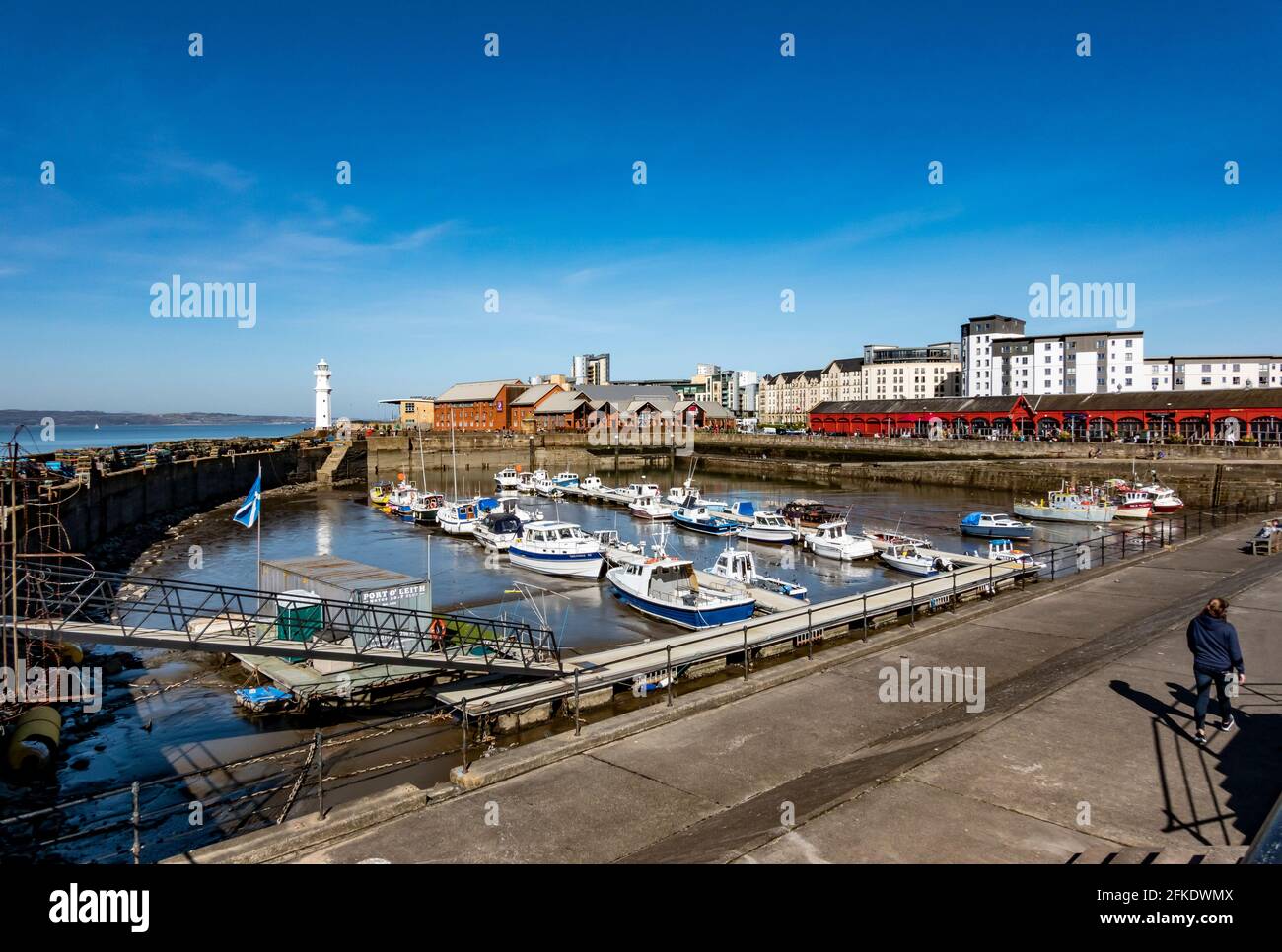 Newhaven Habour, all'estremità ovest del porto occidentale, Leith Docks Edimburgo, Scozia, con faro all'ingresso del porto e barche ormeggiate con bassa marea Foto Stock