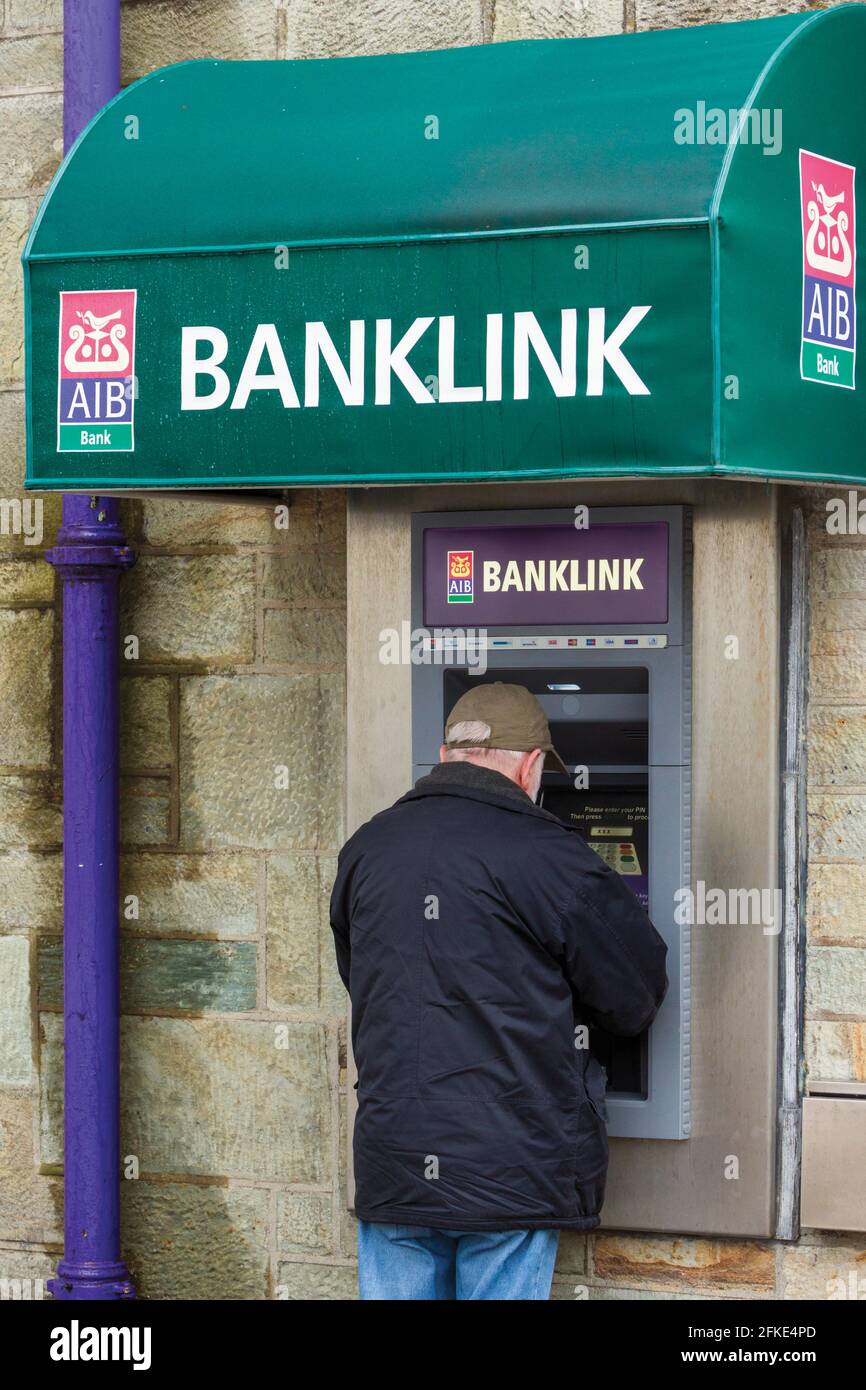 L'uomo che consulta la macchina automatica per la vendita di banconote, o ATM, talvolta denominata "buco nel muro" o bancomat presso una succursale dell'AIB o delle banche irlandesi alleate; Foto Stock