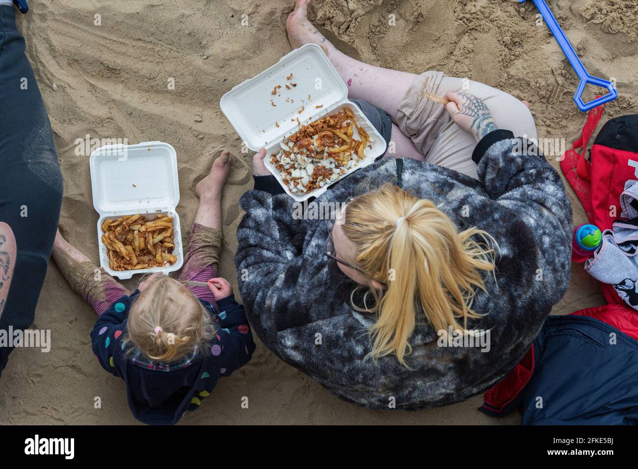 Una giovane famiglia mangia i loro pesci e patatine sulla spiaggia di Hartlepool Headland, Inghilterra, Regno Unito. La famiglia prende il pesce e patatine dal chippy locale. Foto Stock