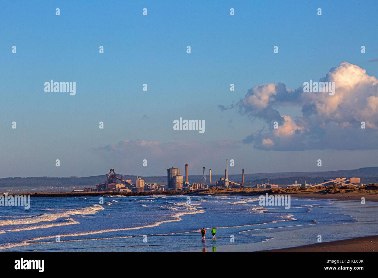 Coppia a piedi lungo la spiaggia con le acciaierie Redcar in distanza, Inghilterra, Regno Unito Foto Stock